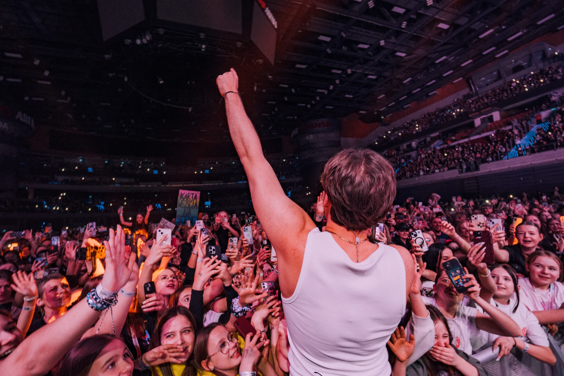 Wokalista Genzie w białym tank topie, odwrócony tyłem do publiczności, z uniesioną ręką w geście triumfu, przed tłumem fanów z telefonami na koncercie Offline tour 2025.