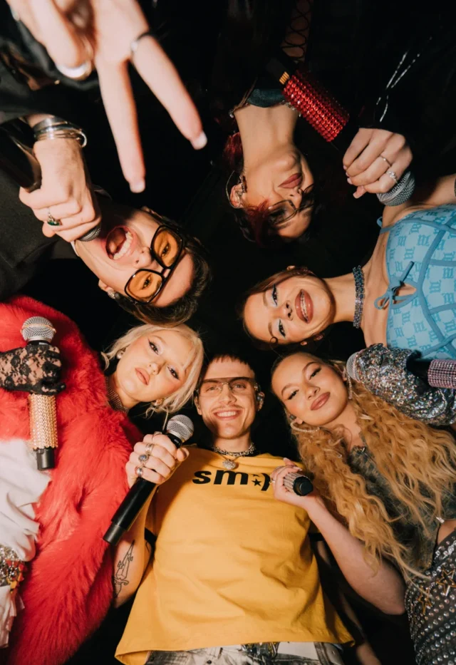 Zespół Genzie w kolorowych strojach, trzymający mikrofony, w ujęciu z dołu tworzy krąg podczas koncertu Offline tour 2025.