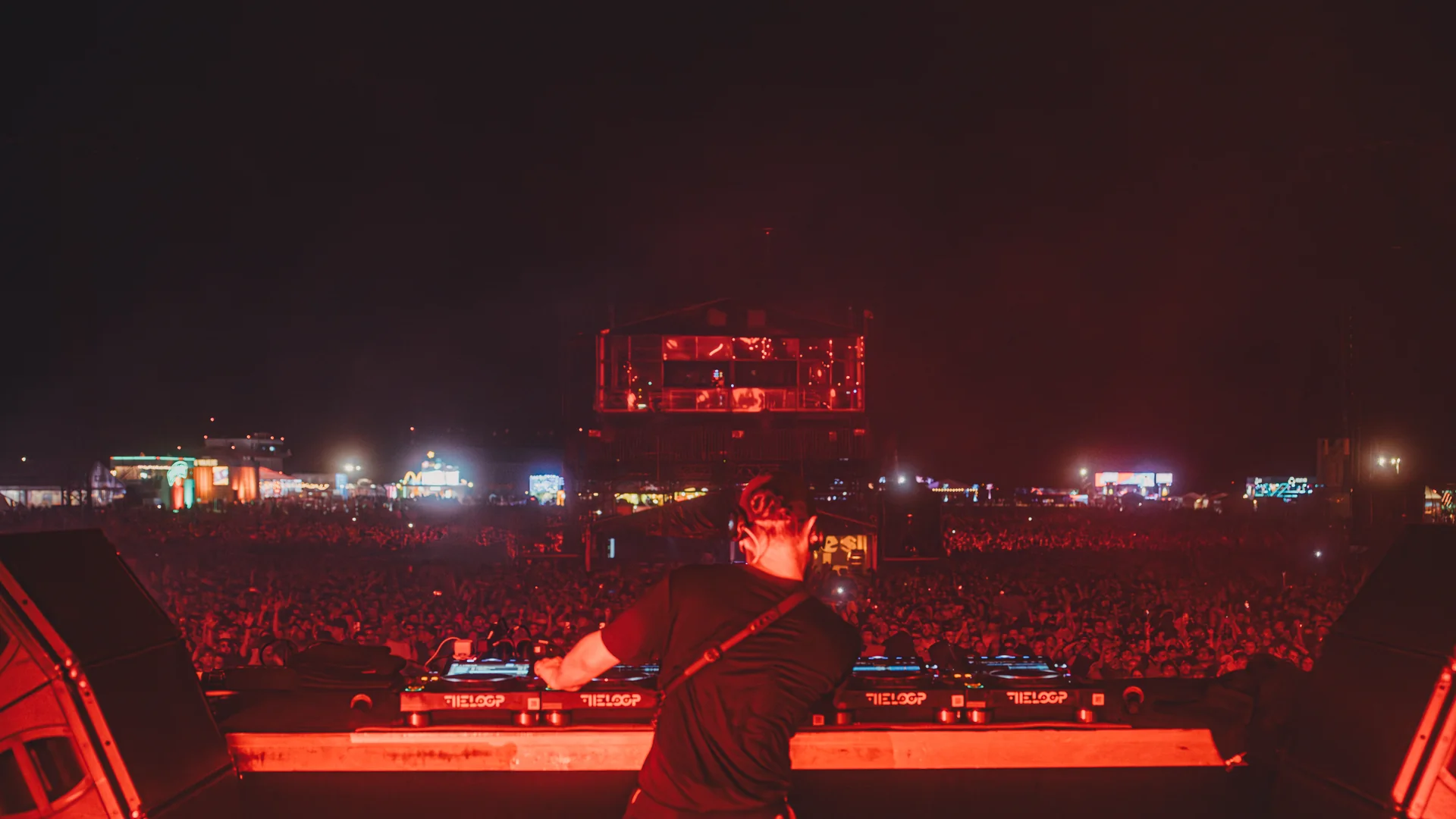 DJ na scenie festiwalu Opener 2024, widziany od tyłu, przed ogromną publicznością oświetloną czerwonymi światłami, podczas nocnego setu.