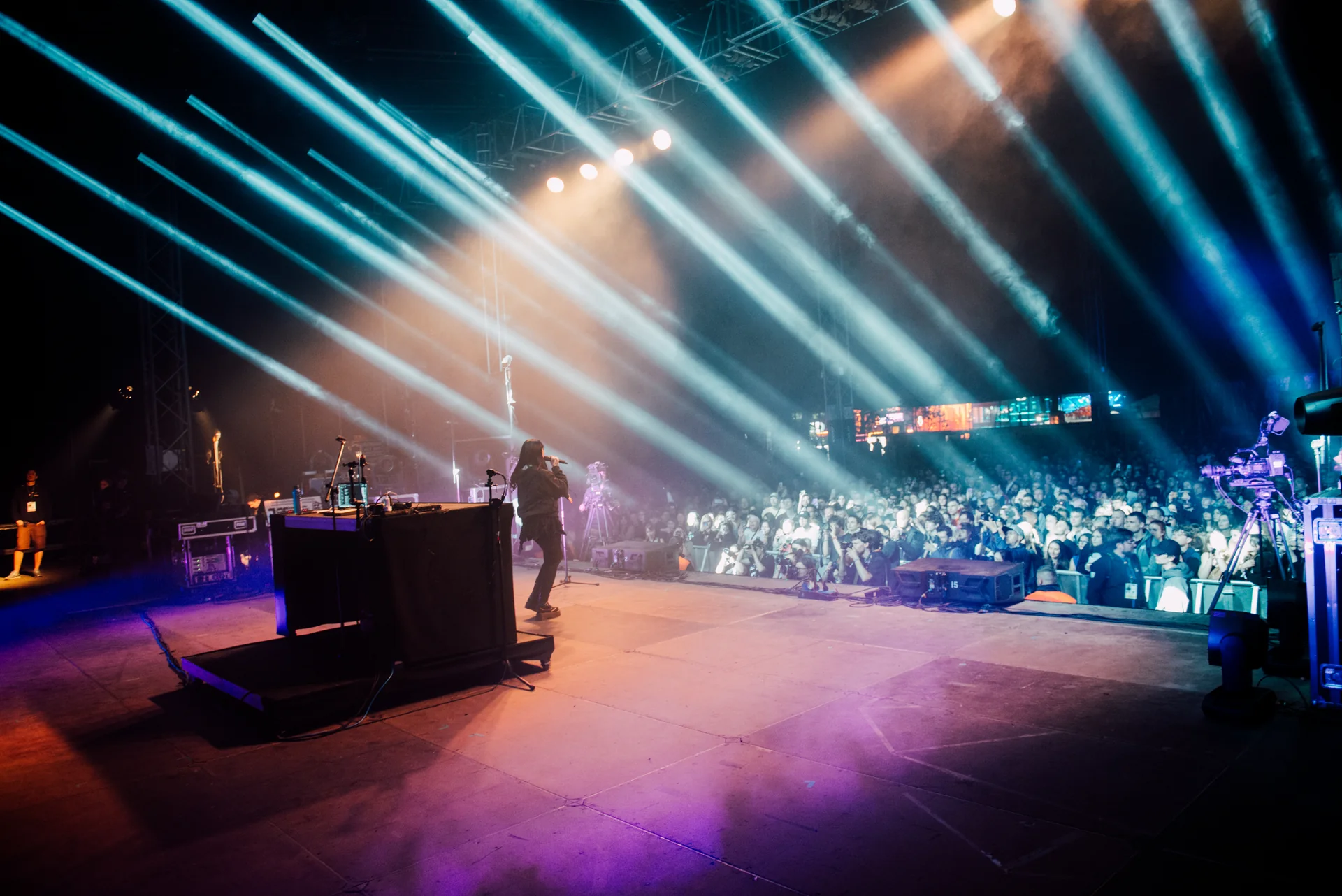 Artysta na scenie Orange Warsaw Festival 2024, śpiewający do mikrofonu, oświetlony jasnymi niebieskimi promieniami światła.