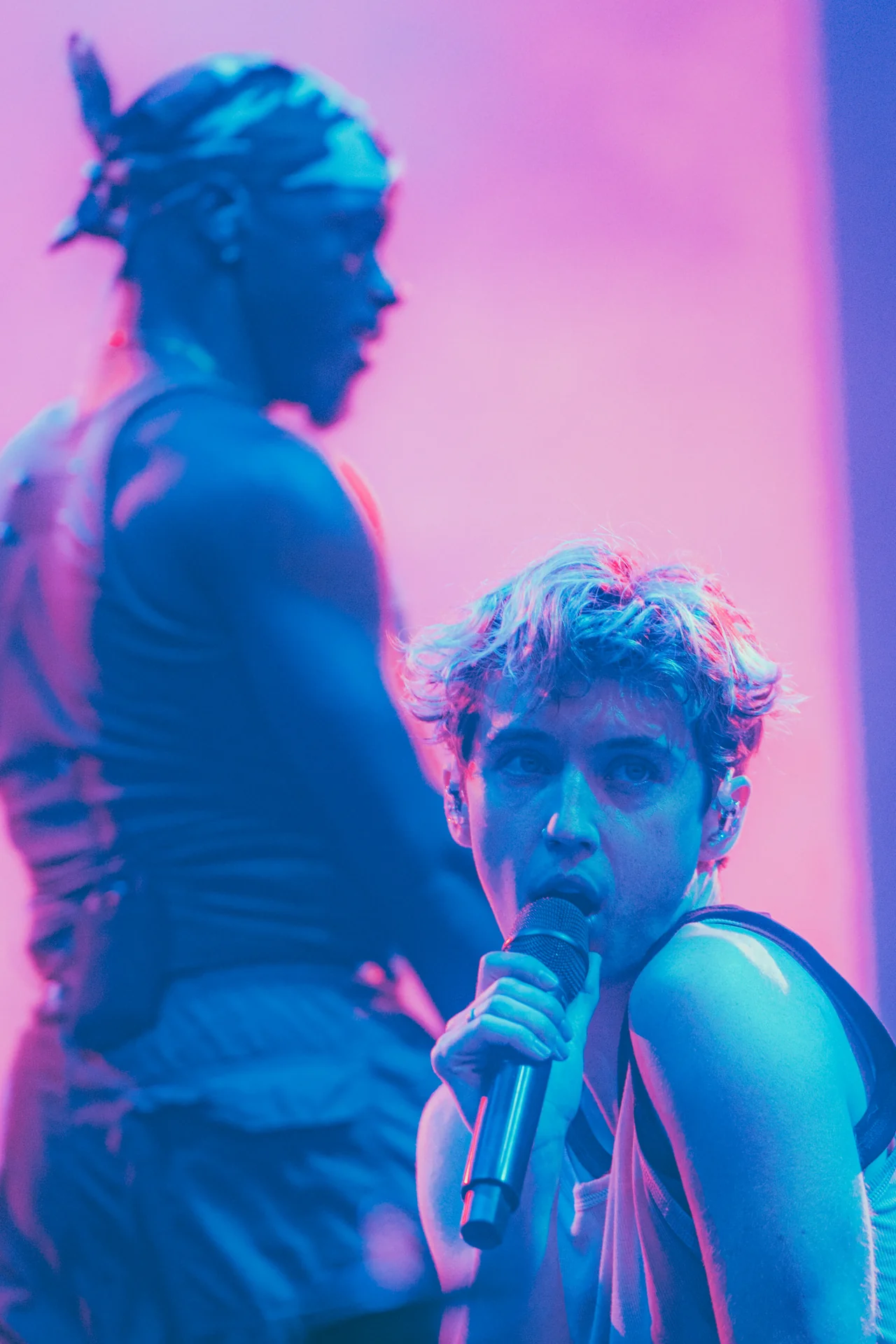 Zbliżenie na Troye'a Sivana śpiewającego do mikrofonu na scenie Orange Warsaw Festival 2024, z tancerzem w tle i niebieskim oświetleniem.
