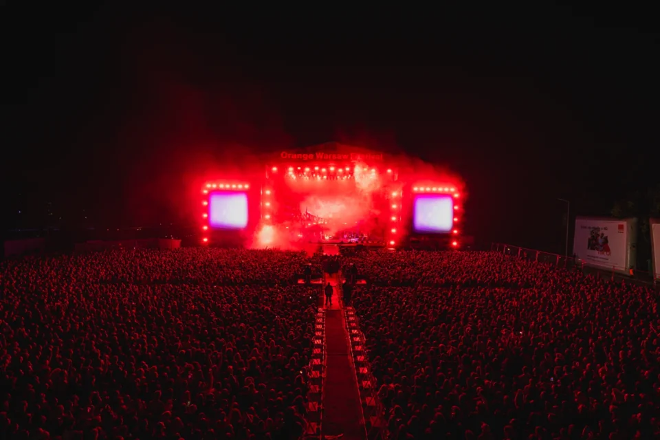 Szeroki kadr głównej sceny Orange Warsaw Festiwal 2025 oświetlonej intensywnym czerwonym światłem, z ogromną publicznością w tle.