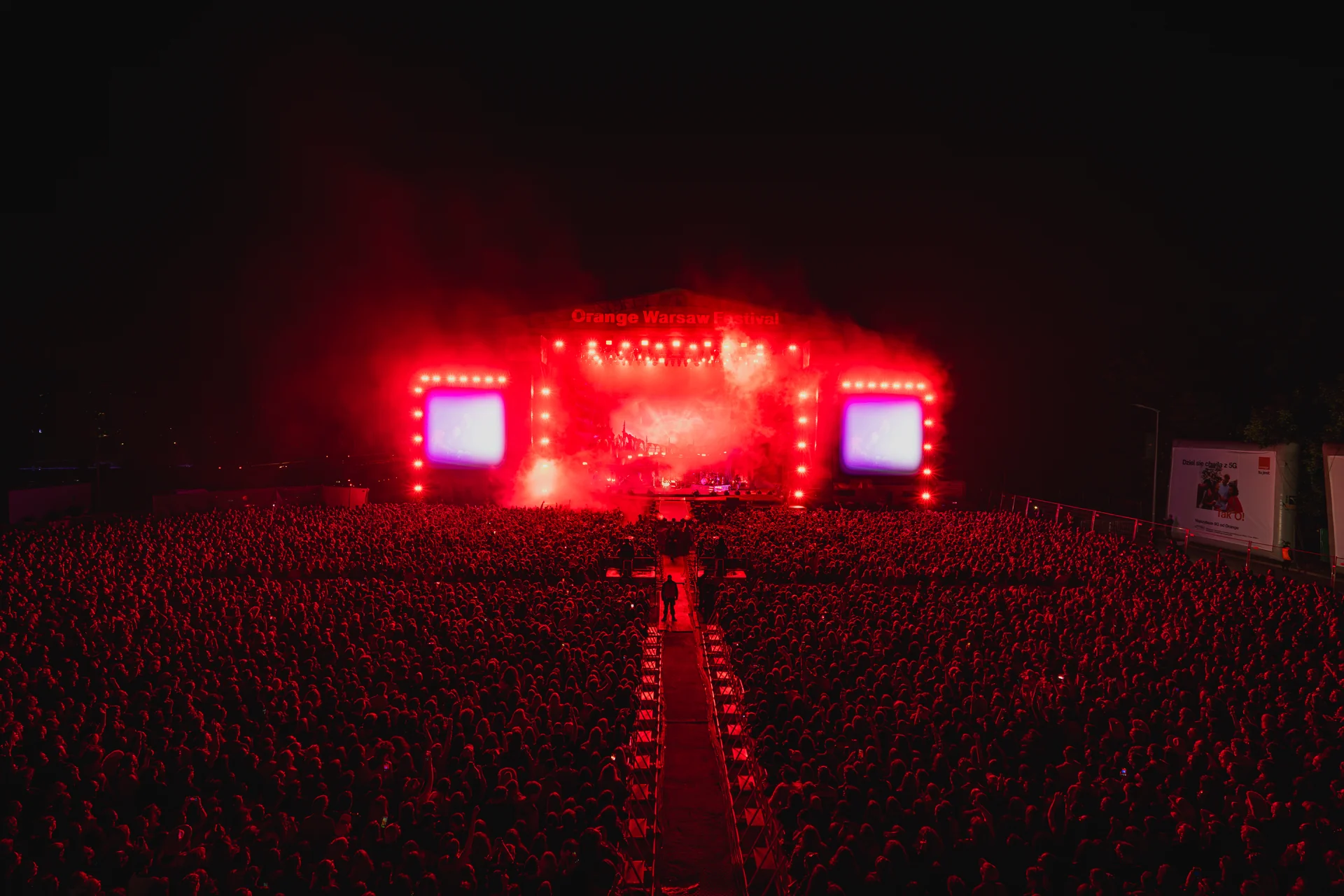 Szeroki kadr głównej sceny Orange Warsaw Festiwal 2025 oświetlonej intensywnym czerwonym światłem, z ogromną publicznością w tle.