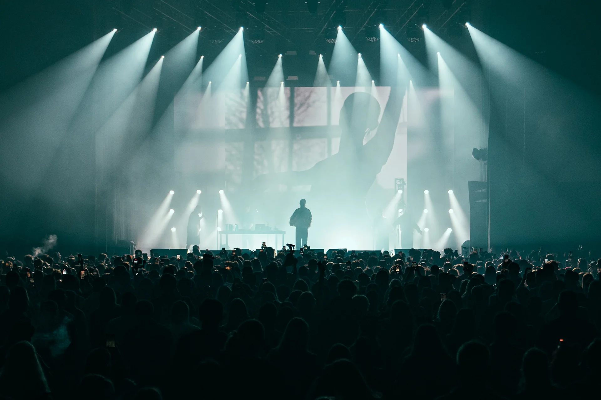 Sylwetka DJ-a za konsolą na scenie Orange Warsaw Festiwal 2025, oświetlona mocnymi promieniami światła z tyłu.