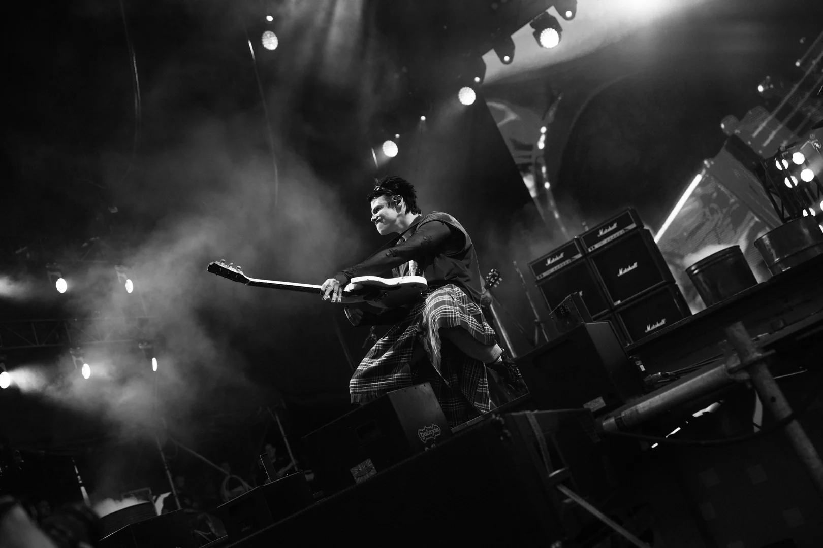 Muzyk w kiltach gra na gitarze, wyrażając intensywne emocje w otoczeniu migających świateł